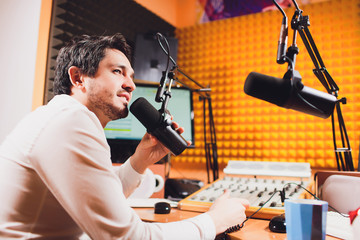 Portrait of handsome young latin man sitting in front of a microphone with laptop at radio station.