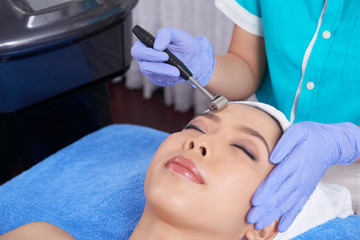 Young Asian woman in towel lying in spa salon enjoying tender face massage