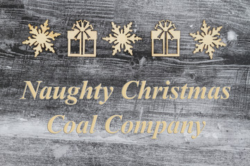 Wooden snowflake and Christmas presents on a weathered wood with text Naughty Christmas Coal Company