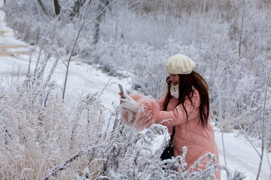 A girl in winter clothes takes pictures of bushes covered with beautiful hoarfrost.
