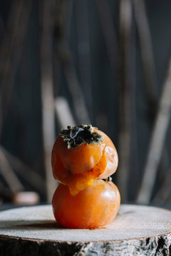 Persimmon fruit on top of another on rustic cutting board