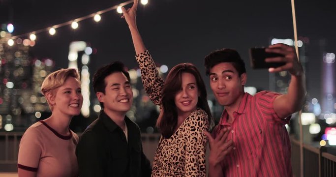 Group of friends taking selfies with city skyline at night