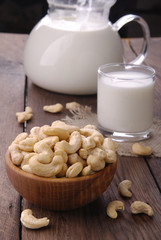 Raw cashews in a wooden bowl and a glass of milk on a wooden background.