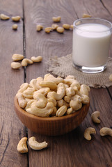 Raw cashews in a wooden bowl and a glass of milk on a wooden background.