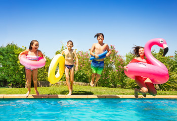Happy teens with swim tools jumping into the pool