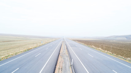 Fototapeta premium Aerial view on speed road, partly covered by fog. Vertical view on rural countryside in autumn, foggy morning. Misty empty road.