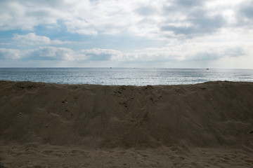 Sand dunes erected to protect buildings built near the beach, the sky is cloudy, over the pile of sand there is the horizon on the sea