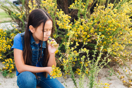 Girl kneeling to smell plant