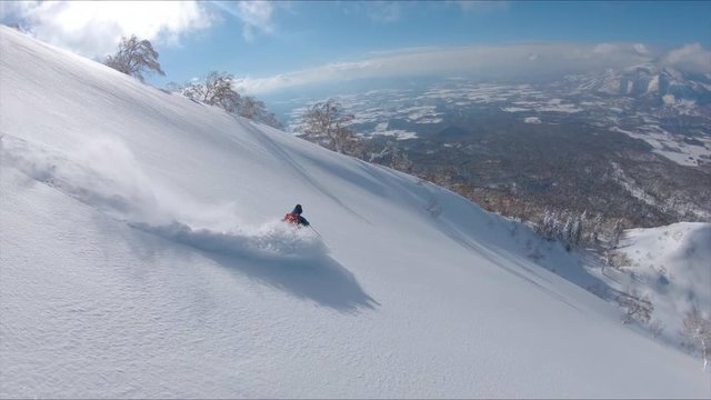 SLOW MOTION, DRONE: Awesome freestyle skier shredding the fresh snow while riding in the scenic mountains in Japan. Flying along the active male tourist skiing downhill in the breathtaking backcountry