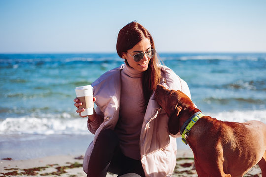 Stylish mid adult woman crouching on beach petting her dog, Odessa, Odeska Oblast, Ukraine