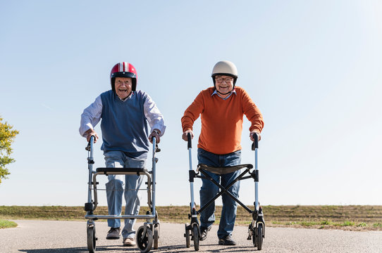 Two old friends wearing safety helmets, competing in a wheeled walker race