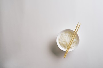 Rice noodles in a plate with chopsticks. Boiled rice noodles in a plate on a white background. Top view