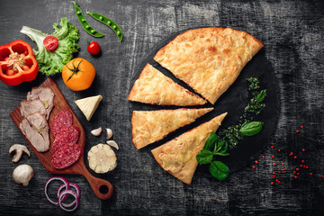 Traditional Italian pizza calzone with ingredients on a stone and dark wooden scratched background