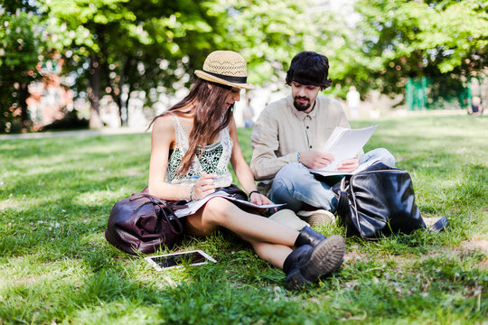 Two students sitting on a meadow in a park looking at notes