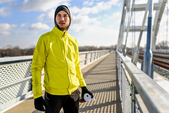 Portrait of young athlete man in windbreaker preparing to exercise on sunny winter day