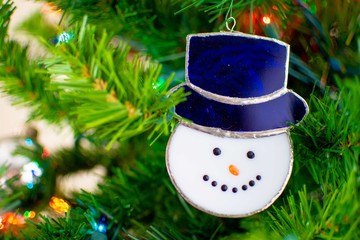 A glass snowman ornament hangs on a Christmas Tree