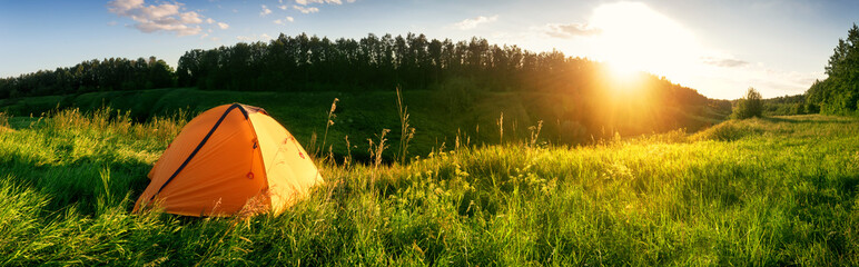 Orange tent in the mountains on a green meadow