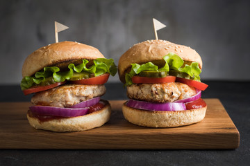 Two homemade turkey burgers with salad, tomatoes, pickles and red onion on wooden cutting board
