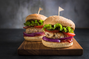 Two homemade turkey burgers with salad, tomatoes, pickles and red onion on wooden cutting board