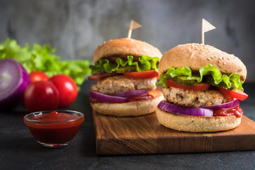 Two homemade turkey burgers with salad, tomatoes, pickles and red onion on wooden cutting board