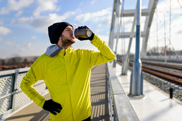Young athlete man drinking water - dehydrating during exercise outdoors.