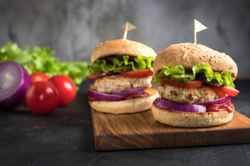 Two homemade turkey burgers with salad, tomatoes, pickles and red onion on wooden cutting board