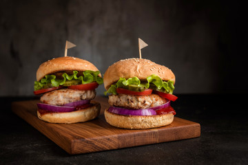 Two homemade turkey burgers with salad, tomatoes, pickles and red onion on wooden cutting board
