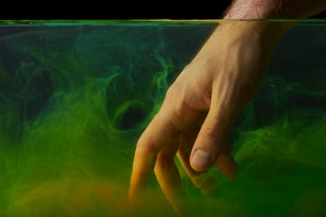 Fototapeta na wymiar partial view of male hand in water with green paint swirls