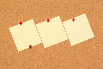 Sticky note pinned on cork board with thumbtacks