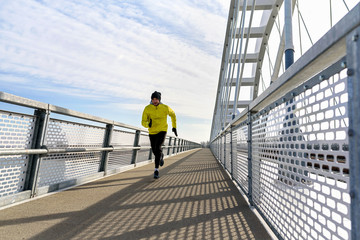 Attractive fit man running fast along big modern bridge. Exercising, Jogging, Sport, Winter. Male athlete running.