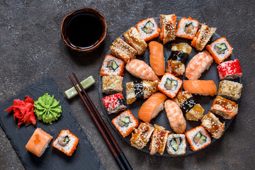 sushi rolls on round slate black Board with wasabi and ginger on dark background