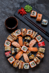 sushi rolls on round slate black Board with wasabi and ginger on dark background