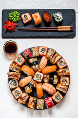 sushi rolls Asian food on round slate black Board with wasabi and ginger, soy sauce on white background with black slate rectangular plate
