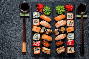 sushi rolls Asian food on rectangular shale plates with wasabi and ginger, with chopsticks and soy sauce on a dark background