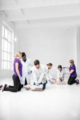 Fototapeta premium Group of young medics practising to make artificial breathing with medical dummies during the first aid training in the white room