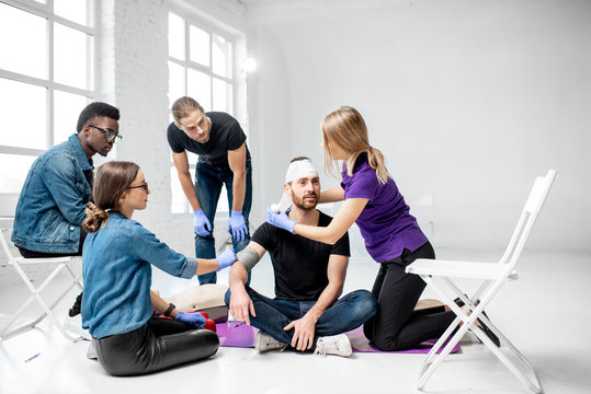 Group of young people during the first aid training with instructor showing how to tie a bandage on the head of injured person