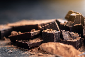 Pieces of dark bitter chocolate with cocoa powder on dark wooden background. Concept of...