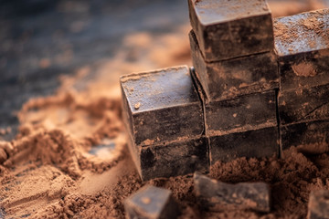 Pieces of dark bitter chocolate with cocoa powder on dark wooden background. Concept of confectionery ingredients