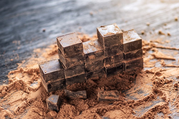 Pieces of dark bitter chocolate with cocoa powder on dark wooden background. Concept of confectionery ingredients