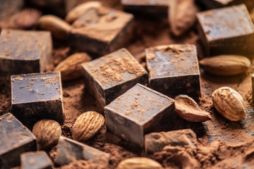 Pieces of dark bitter chocolate with cocoa and almonds nuts on wooden background. Card with space for text