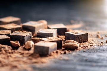 Pieces of dark bitter chocolate with cocoa and almonds nuts on wooden background. Card with space...
