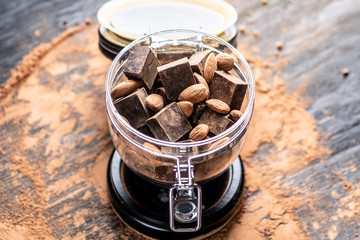 Pieces of dark bitter chocolate with cocoa and nuts almonds on wooden background. Concept of confectionery ingredients