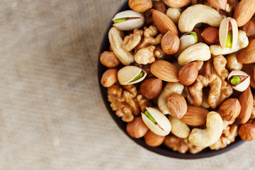 Mix of different nuts in a wooden cup against the background of fabric from burlap. Nuts as structure and background, macro. Top view.