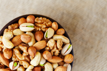 Mix of different nuts in a wooden cup against the background of fabric from burlap. Nuts as structure and background, macro. Top view.