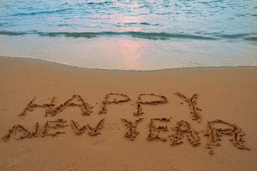 Happy new year concept handwriting on the sand beach.