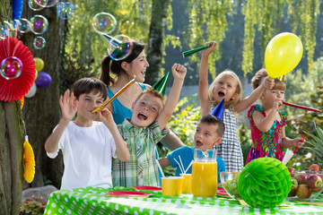 Kids in birthday hats and playing with balloon during garden party