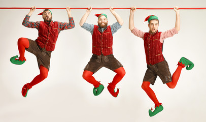 The happy smiling friendly men dressed like a funny gnome or elf hanging on an isolated gray studio...