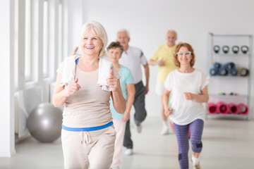 Happy active senior woman with towel exercising during physical classes for elderly people