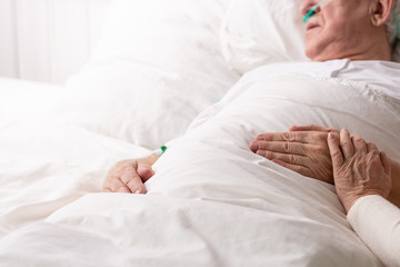 Senior man with terminal illness laying in hospital bed, helping and on his hand as symbol of support, photo with copy space