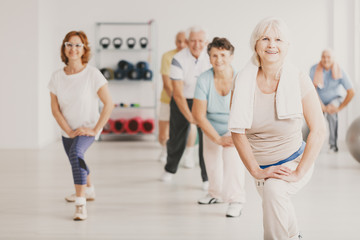 Smiling senior woman with towel exercising during yoga classes for elderly people